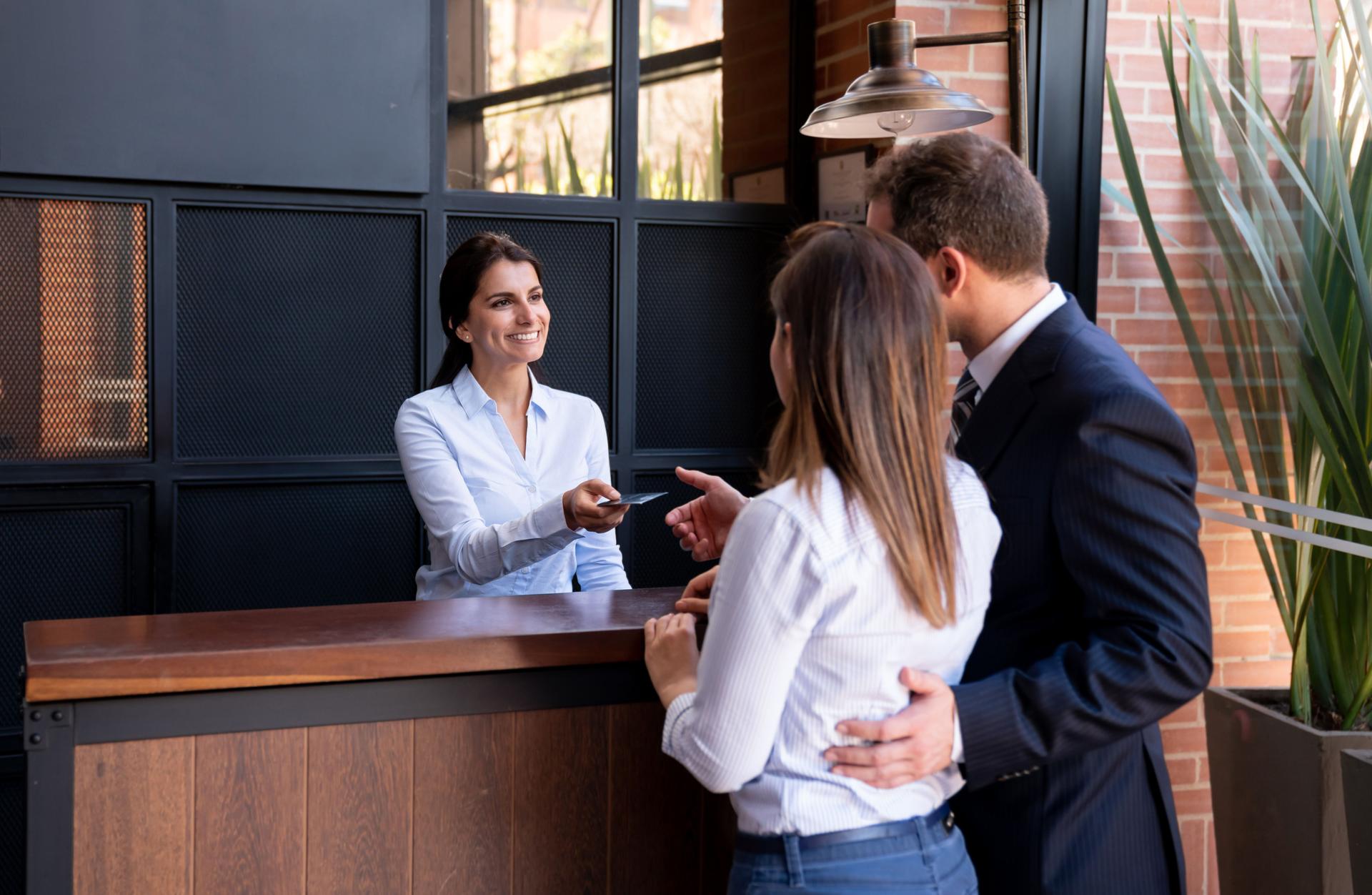 Friendly receptionist handing a guest business couple the key to their room at a luxury hotel