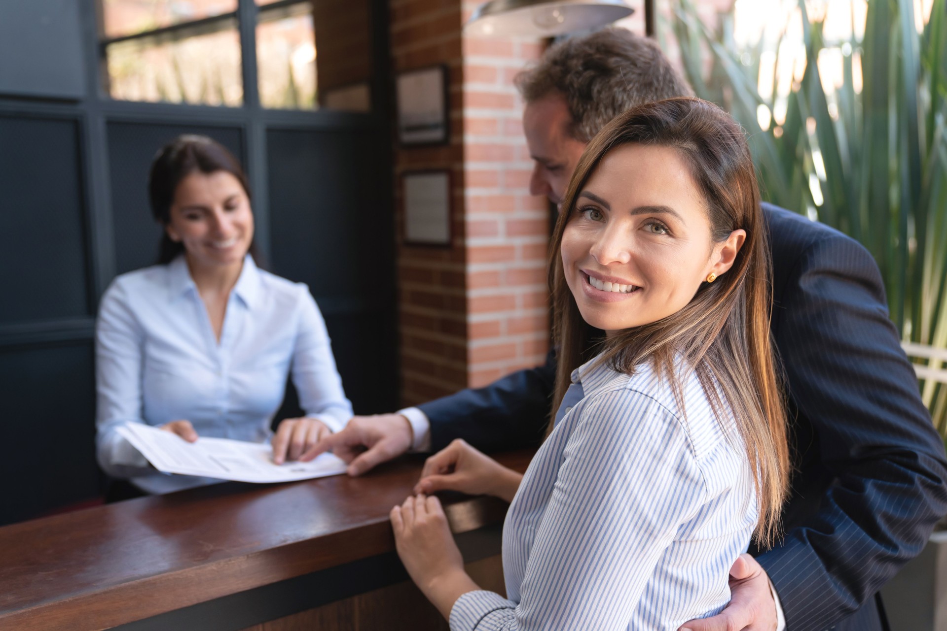 Belle femme d'affaires faisant face au sourire d'appareil-photo tandis que le partenaire prend soin de la paperasse à l'enregistrement avec le réceptionniste dans un hôtel de luxe
